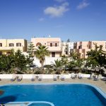 Maistros Village Santorini ana havuz, şezlong dizilimi, Santorini renkli ev cepheleri arka planda