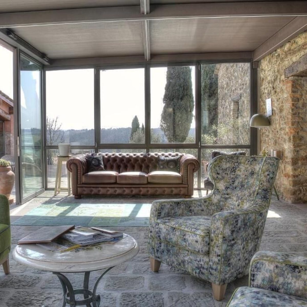 Salvadonica Borgo del Chianti otel taş duvarlı oturma salonu ve cam cepheden Toskana kırsalı manzarası, Chianti