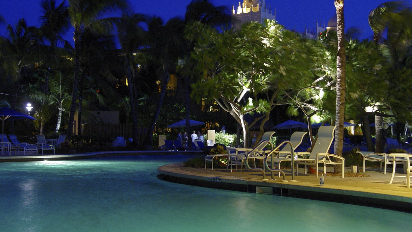 Gece aydınlatılmış resort havuzu, palmiyeler ve havuz kenarı şezlonglar
