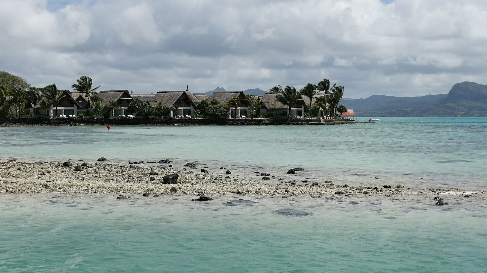 Mauritius'ta turkuaz lagün kıyısında sazdan çatılı resort villaları ve arkada dağlar