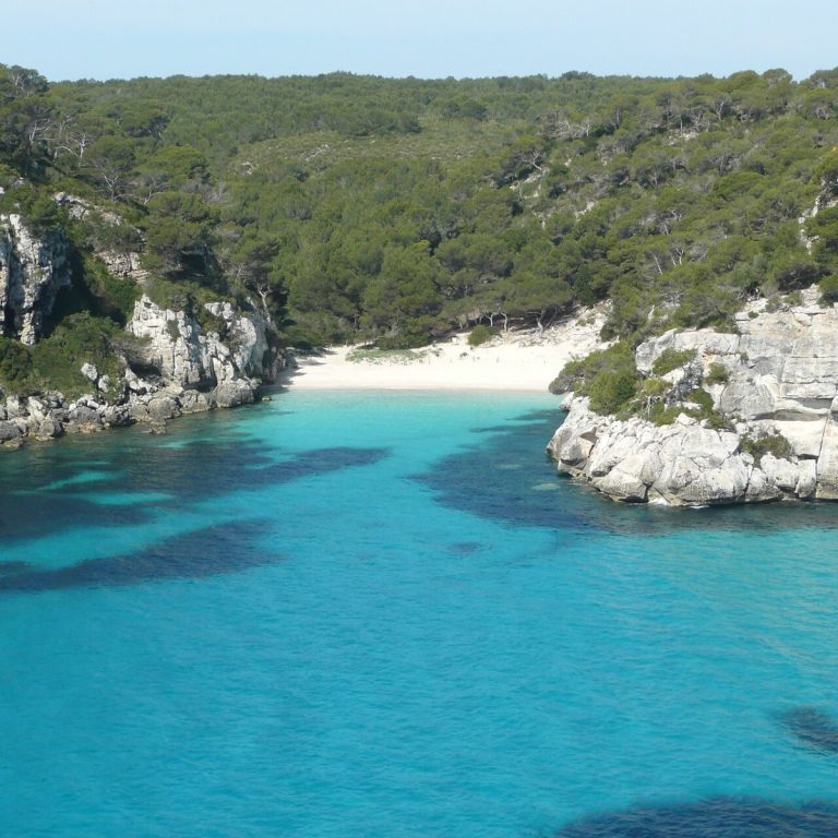 Menorca turunda Cala Macarelleta koyunun kayalıklar arasındaki berrak turkuaz denizi